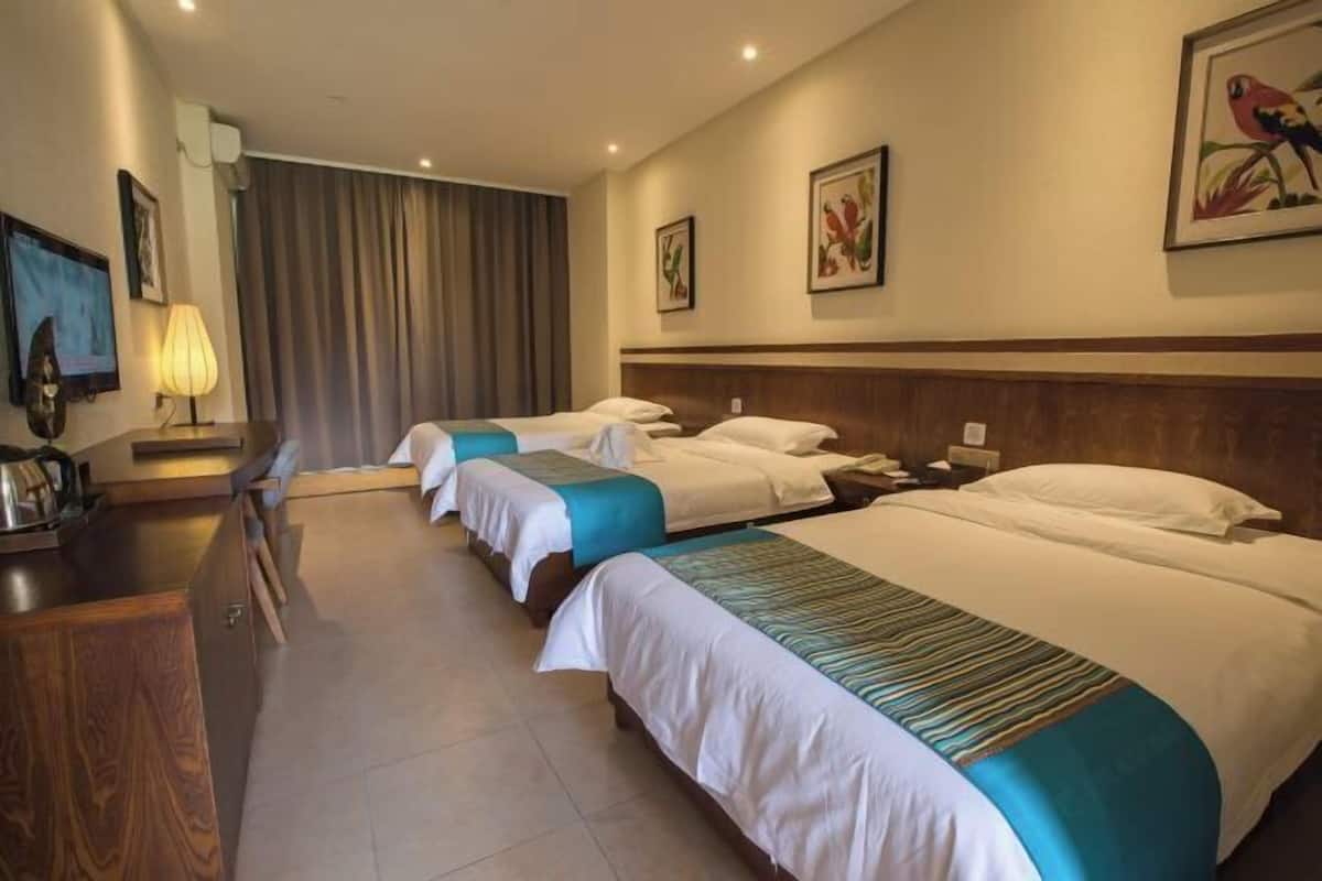 Quarto de hotel com três camas, uma escrivaninha com luminária e obras de arte nas paredes.