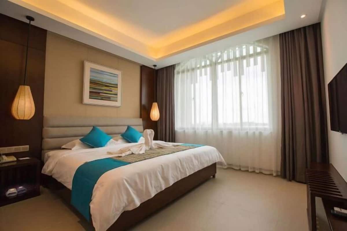 Quarto de hotel com uma cama grande, um quadro na parede e uma televisão à direita.