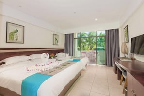 A hotel room with a bed, a desk, a chair, a balcony with a view of greenery, and artwork on the walls. - Longxing Lehman Sea View Resort (Sanya)