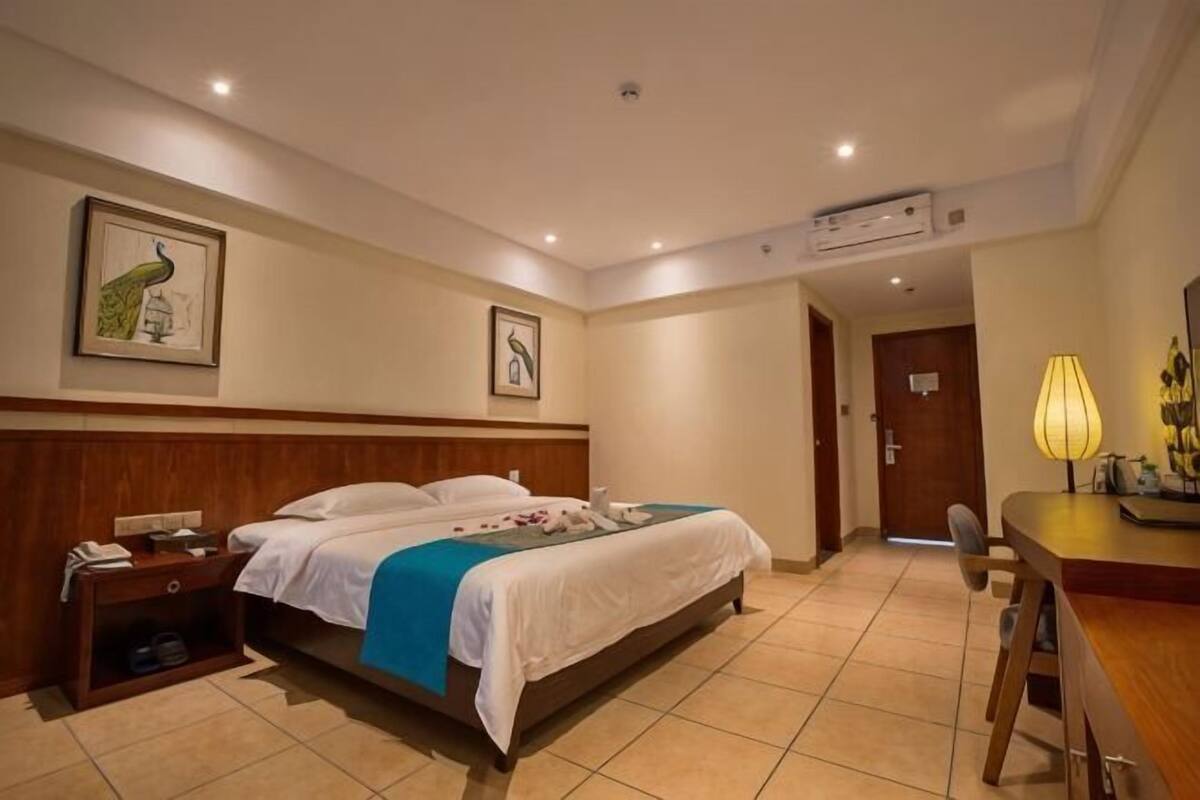 Quarto de hotel com cama, mesa de cabeceira, abajur e obra de arte na parede.