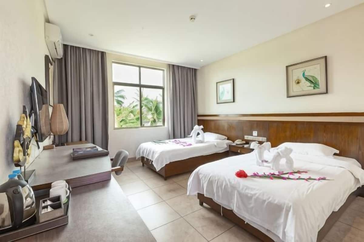 Quarto de hotel com duas camas, uma mesa, uma cadeira, televisão e janela com cortinas.