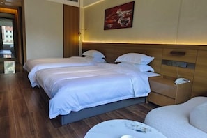 Una habitación de hotel con dos camas, una mesita de noche, una mesa redonda y un cuadro en la pared.