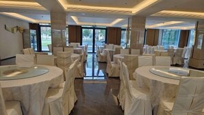 A banquet hall with round tables covered in white tablecloths and chairs, large windows, and a modern interior design.