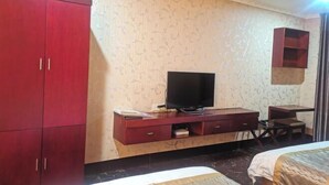 A hotel room with a large wardrobe, a TV on a wooden cabinet, a desk with a chair, and a bed.