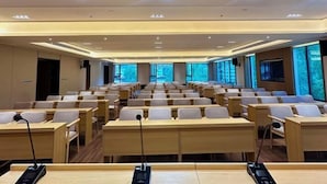 A conference room with rows of desks and chairs, equipped with microphones and a projector.