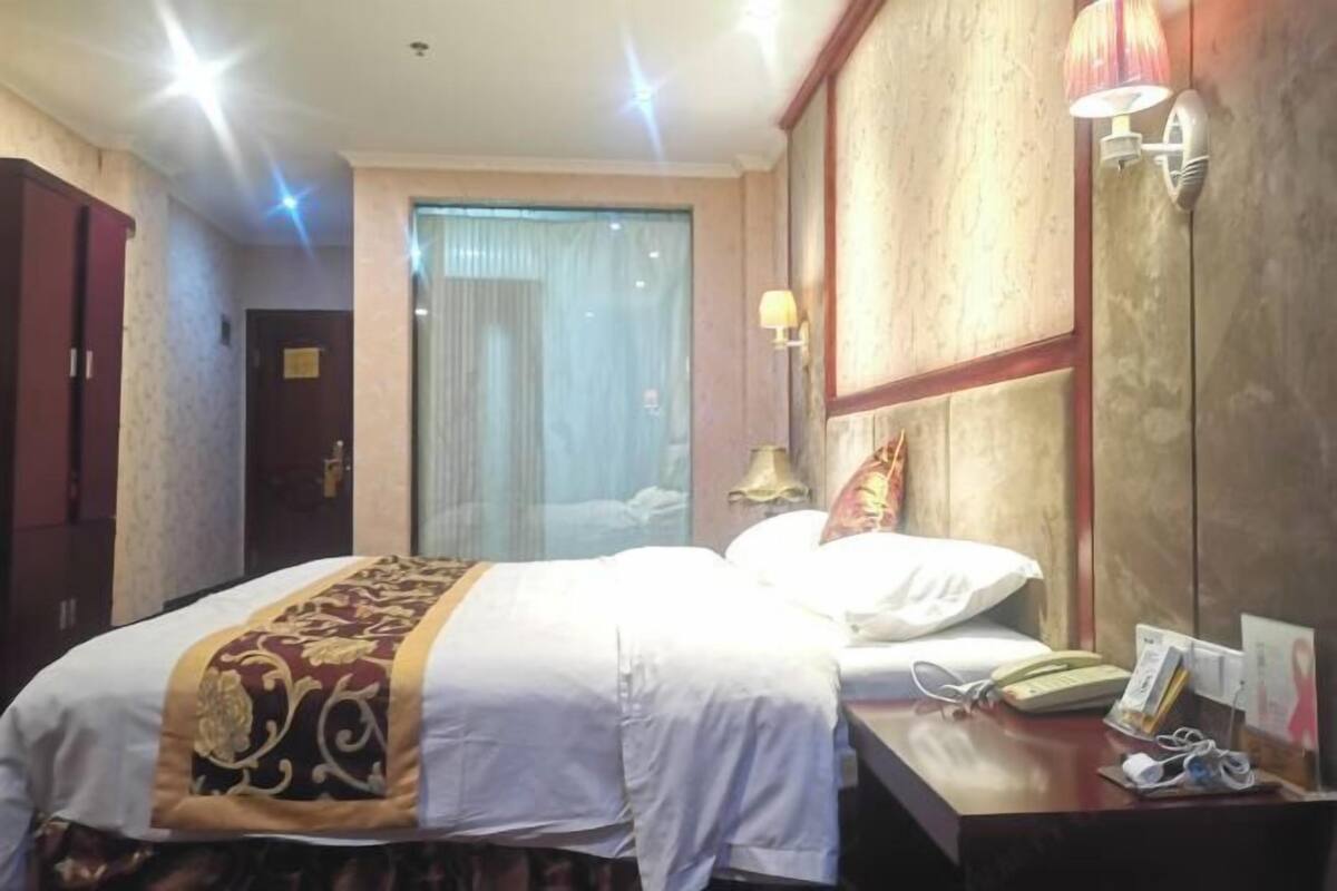 Quarto de hotel com cama, mesa de cabeceira, abajur e janela com cortinas.