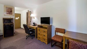 Et lille hotelværelse med skrivebord, fjernsyn, mikroovn, stol og kommode.