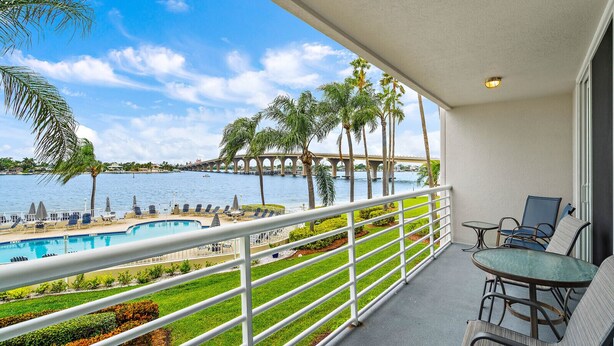 Un balcon avec vue sur une piscine, des palmiers et un pont.