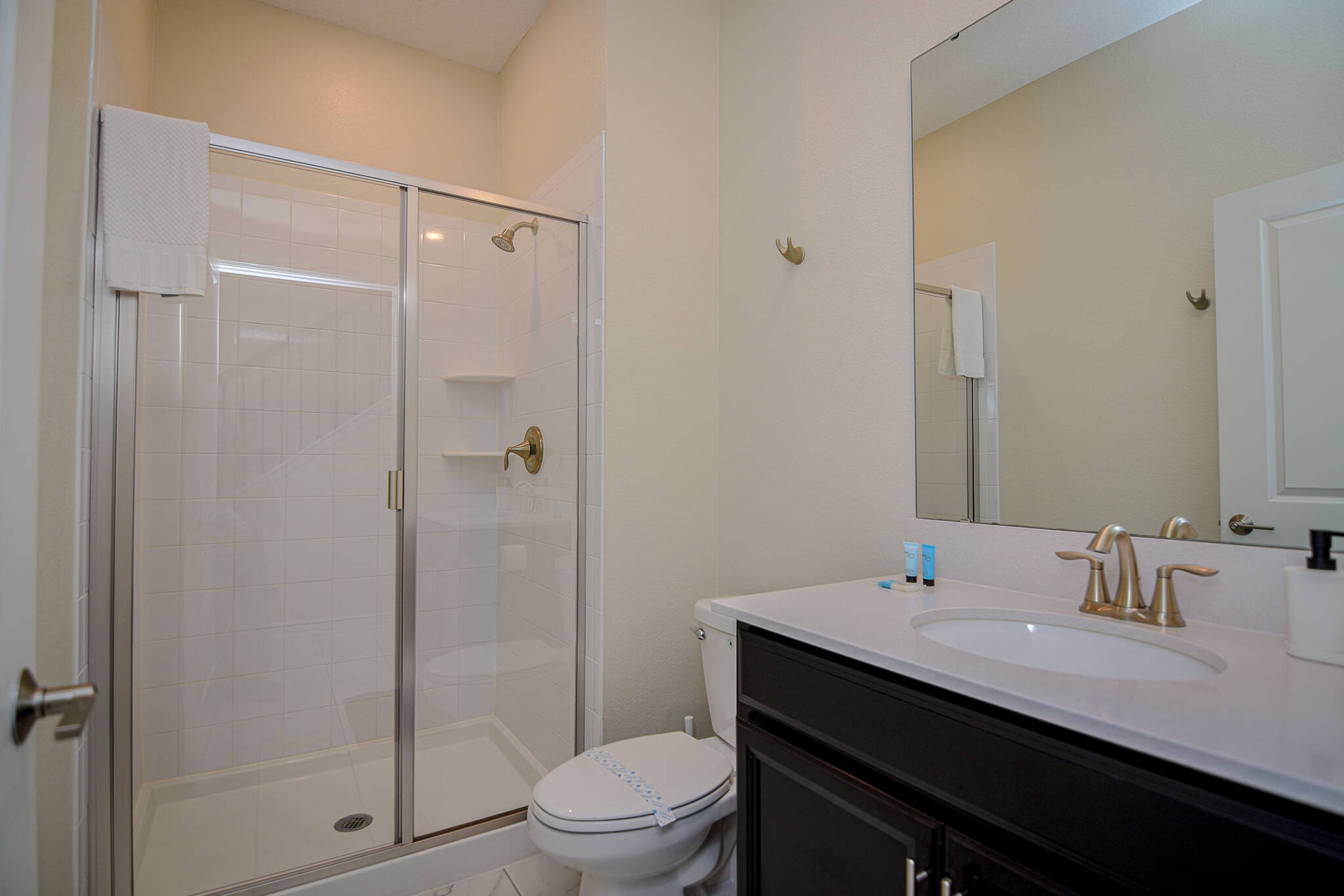 A bathroom with a glass-enclosed shower, a white toilet, and a sink with a gold faucet.