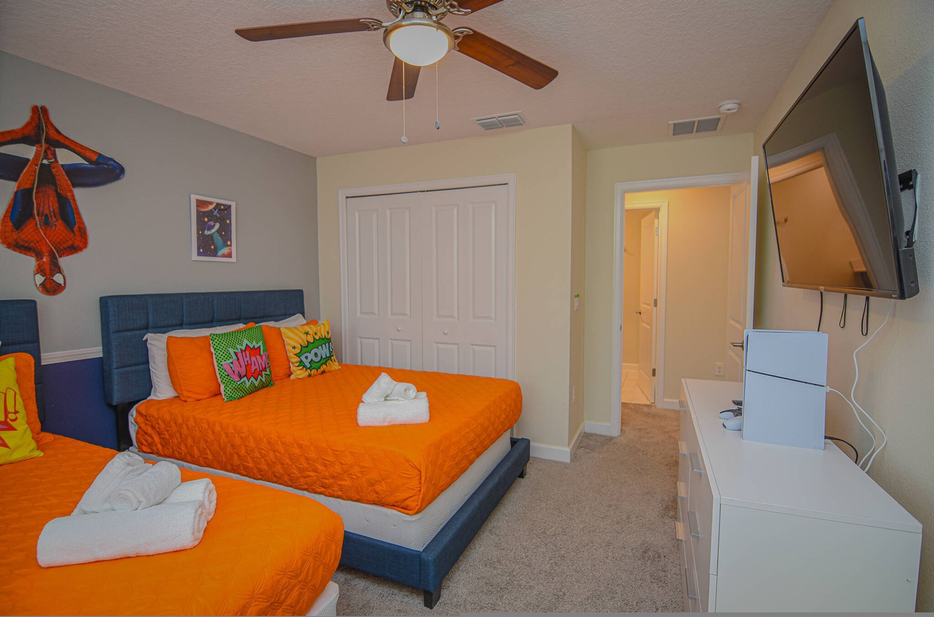 A hotel room with two beds, a ceiling fan, a television, and a door leading to another room.