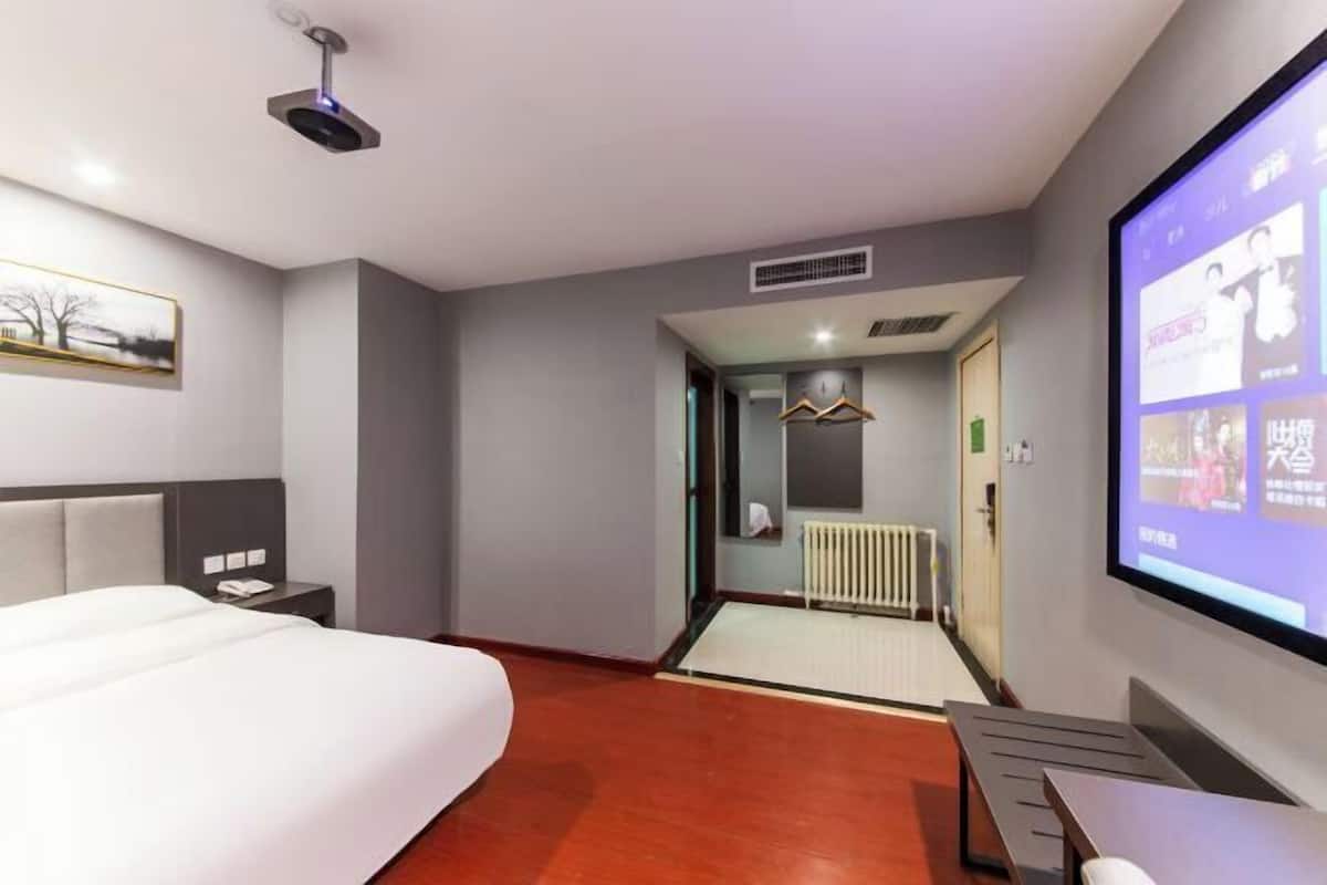 Quarto de hotel com uma cama, uma secretária, um ecrã de projetor e vista para o corredor.