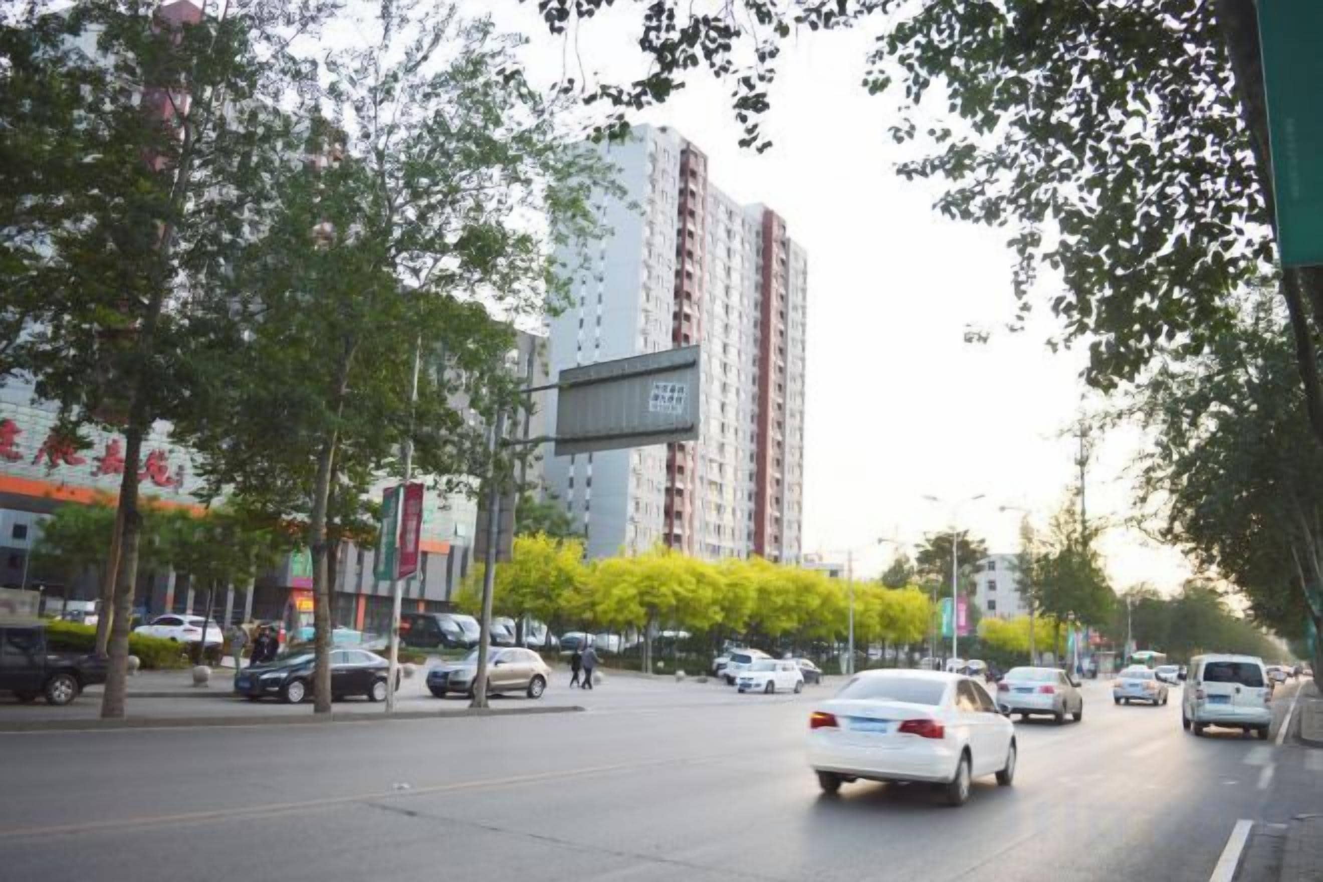 A street with cars, trees, and a tall building in the background.
