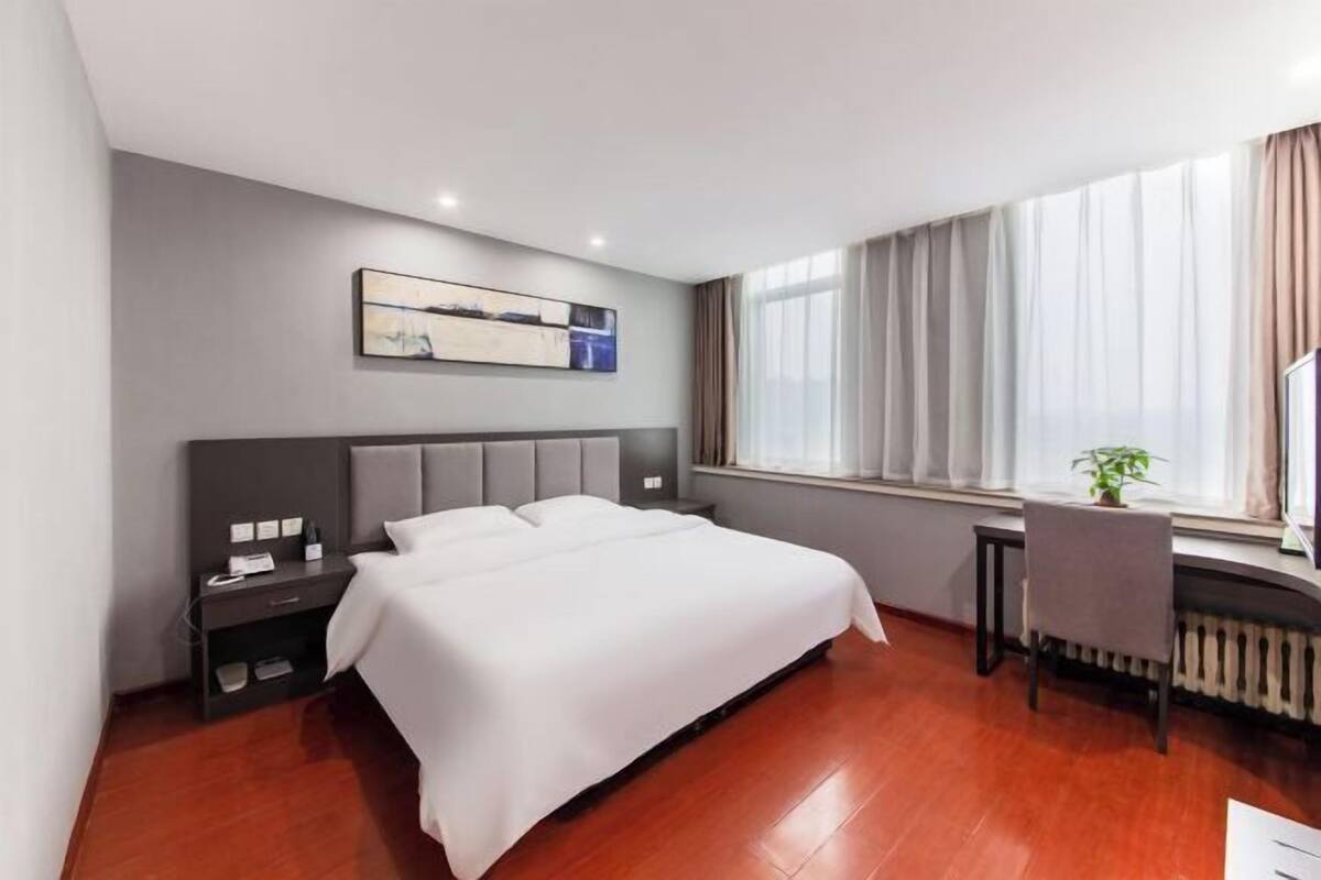 Quarto de hotel moderno com uma cama grande, uma escrivaninha e uma janela com cortinas.