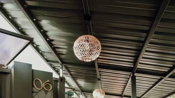 A covered corridor with wooden flooring, metal railings, and hanging spherical light fixtures.