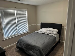 Ein Schlafzimmer mit einem Bett, einem Fenster mit Jalousien und einem Teppichboden.