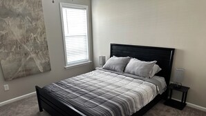 Een slaapkamer met een bed, nachtkastje, wandlamp en een raam met jaloezieën.