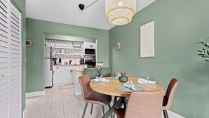 A modern kitchen with white cabinets, a microwave, and a sink. There is a dining area with a round table, chairs, and a hanging light fixture. - Private Garden Apartment with Heated Pool 1BR (Sarasota)
