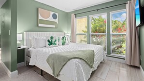 A bedroom with a bed, a nightstand, a TV, and a window with blinds. - Private Garden Apartment with Heated Pool 1BR (Sarasota)