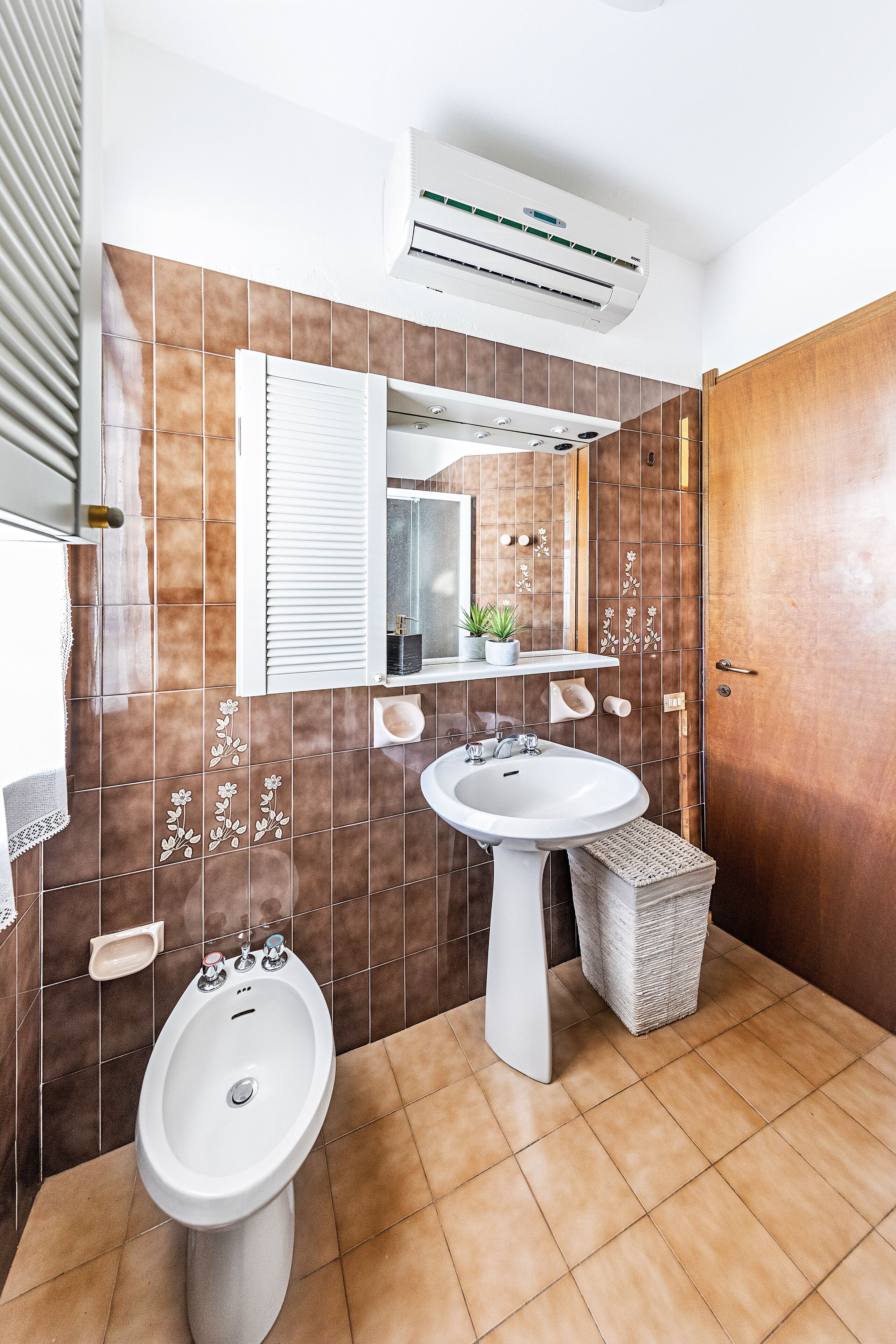 A bathroom with a pedestal sink, a bidet, and a mirror above the sink.
