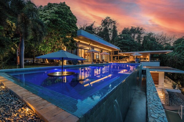 A modern pool area with a clear pool, lounge chairs, and umbrellas.