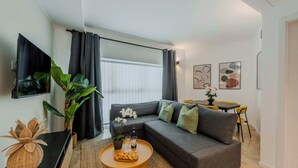 En moderne stue med en grå sofa, gule lænestole, et rundt sofabord og et fjernsyn ophængt på væggen.