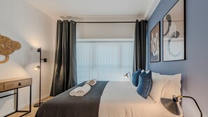 Et moderne hotelværelse med seng, sengebord, lampe og et vindue med gardiner.