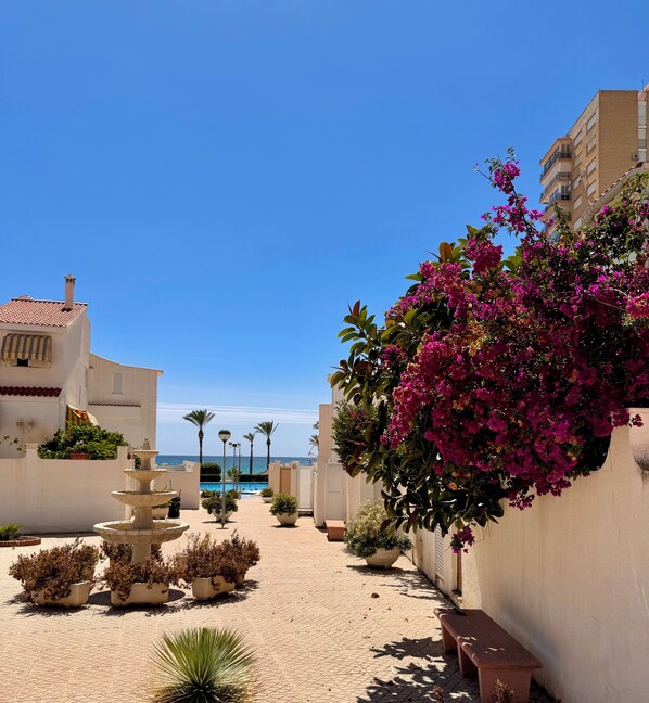 Un patio con una fuente, plantas en macetas y vista al mar.