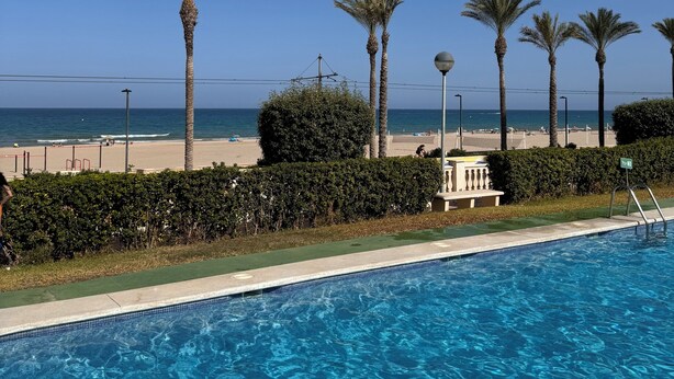 Una piscina con agua cristalina azul, rodeada de palmeras y vista a la playa y al océano.