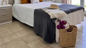 Un dormitorio moderno con una cama grande, mesitas de noche, un velador y un ventilador de techo, con vistas al exterior a través de una puerta corrediza de vidrio.