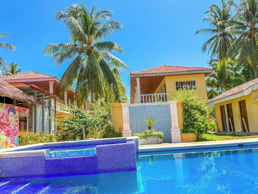A poolside view of a resort with a tiled pool, palm trees, and a building with a tiled exterior.