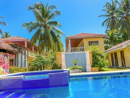 A poolside view of a resort with a tiled pool, palm trees, and a building with a tiled exterior.