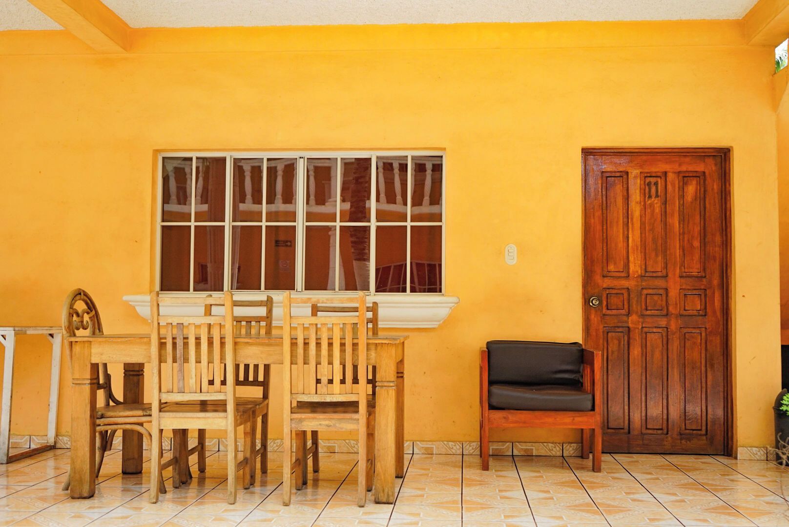 Una habitación con una mesa y sillas de madera, un banco, un ventanal grande y una puerta de madera.