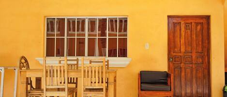 Una habitación con una mesa y sillas de madera, un banco, un ventanal grande y una puerta de madera.