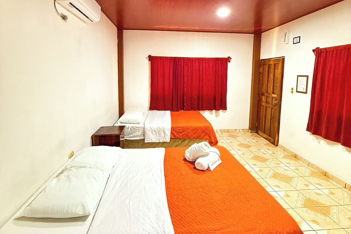 A hotel room with two single beds, a wooden ceiling, red curtains, and a tiled floor.