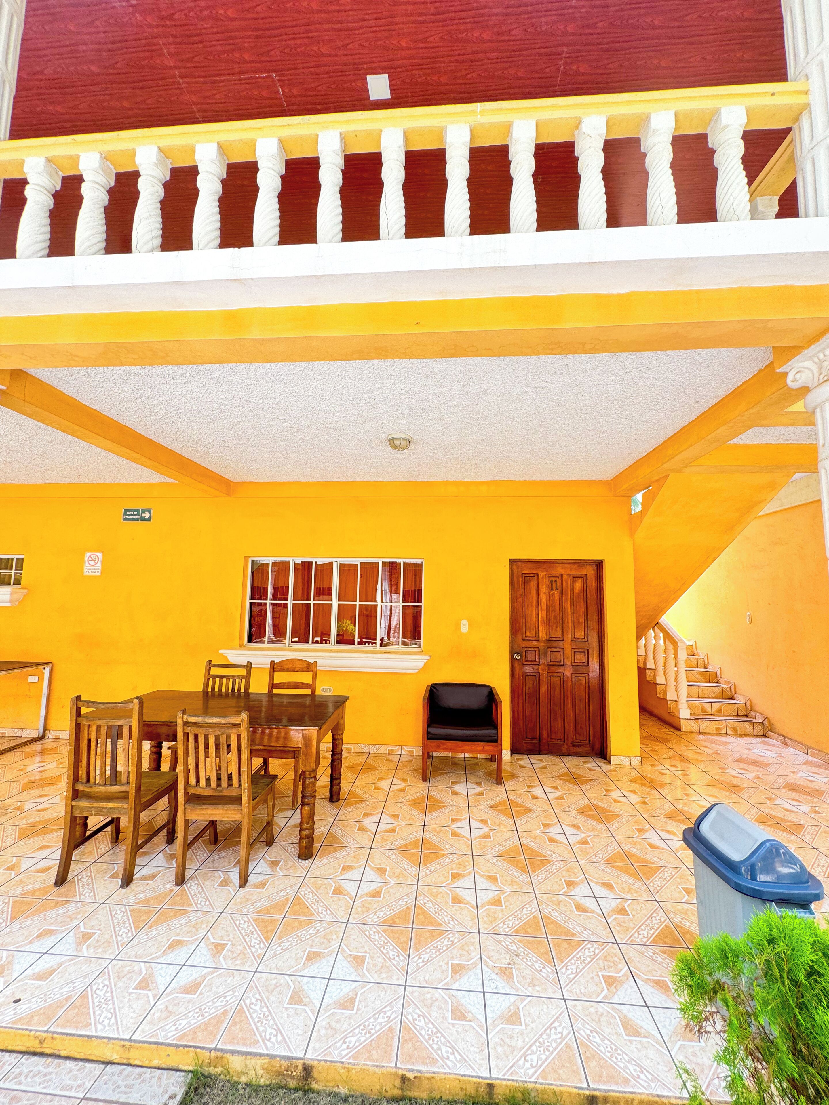 Un comedor con una mesa y sillas, una ventana con cortinas, una puerta y una escalera que sube a un nivel superior.
