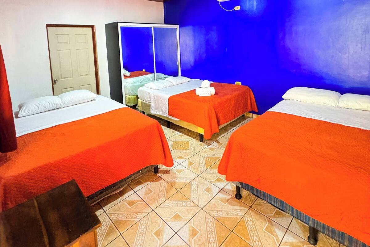 A hotel room with three beds, a wooden ceiling, a blue wall, and an air conditioning unit.