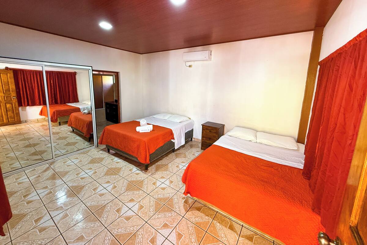 A hotel room with two beds, a small wooden nightstand, a mirror, and a red curtain.