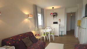 A compact living space with a patterned sofa, a small dining table, and a kitchenette. - Les rives des Issambres 1201 (Roquebrune-sur-Argens)