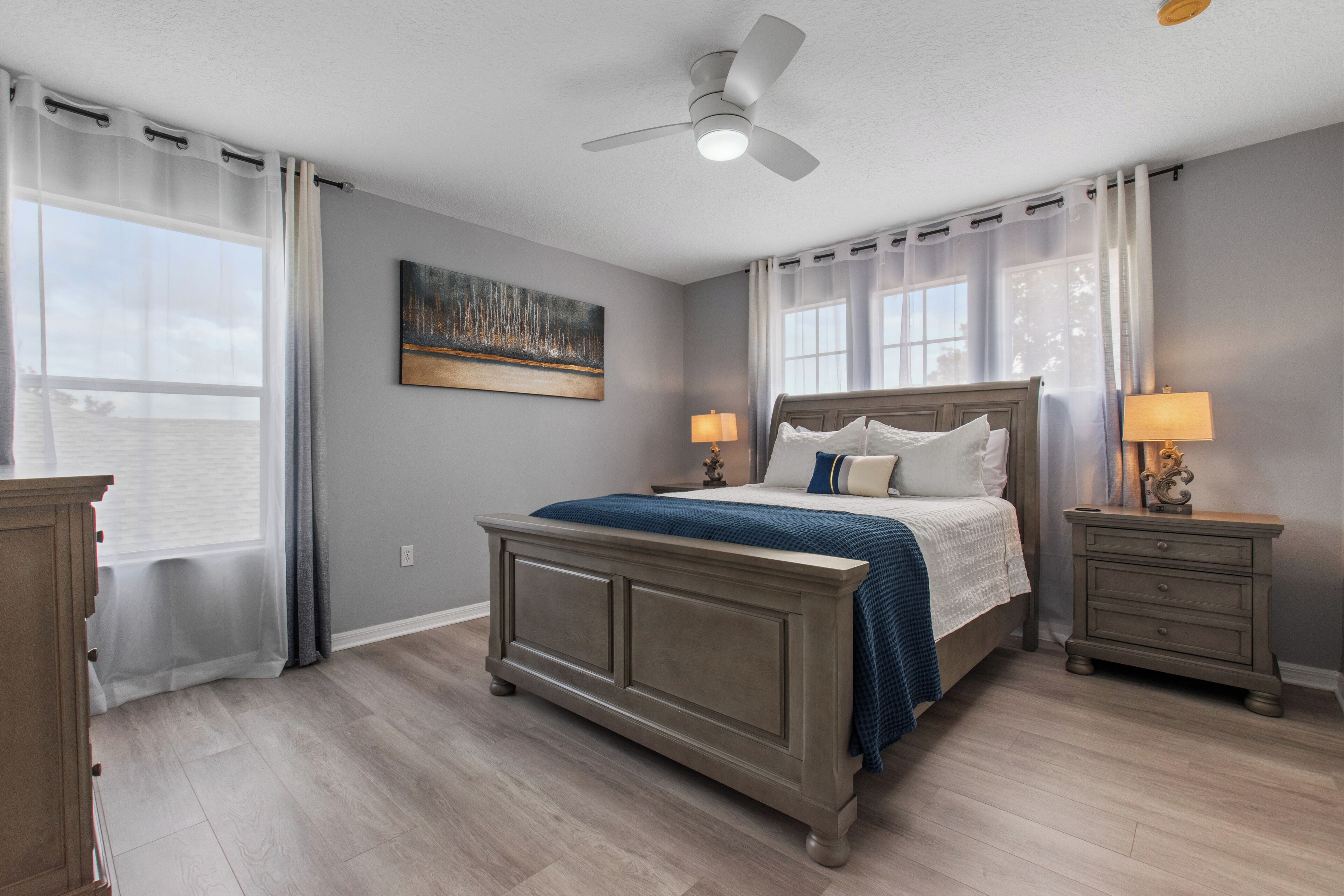 A bedroom with a bed, nightstands, a ceiling fan, and a window with curtains.