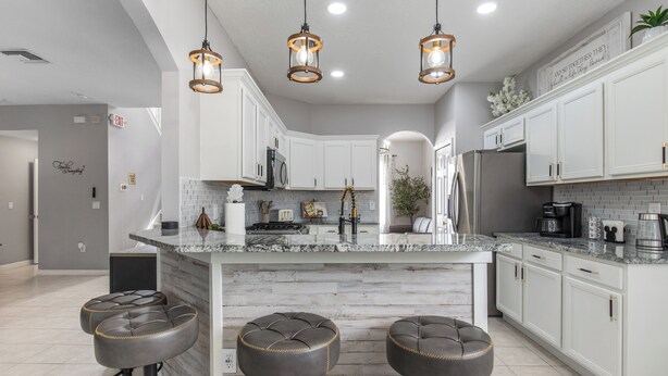 A modern kitchen with white cabinets, a marble island, and three bar stools. - Luxury relaxing stay. A brand new remodel villa near Disney and Legoland  (Haines City)