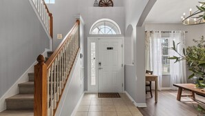 A clean, well-lit hallway with a wooden staircase, a white door with a welcome mat, and a dining area with a table and chairs. - Luxury relaxing stay. A brand new remodel villa near Disney and Legoland  (Haines City)