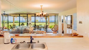 A modern kitchen with a large island, a double sink, and a view of the ocean through large windows. - Ocean & Golf Views | Remodeled Kona Villa w/ AC (Kailua-kona)