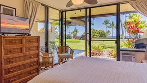 A hotel room with a large bed, a television, wicker furniture, and a view of the outdoors. - Ocean & Golf Views | Remodeled Kona Villa w/ AC (Kailua-kona)