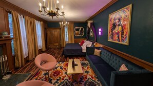 A room with a chandelier, a sofa, a chair, a bed, a mirror, and a colorful painting on the wall. - Spacious King Suite! Cher inspired unit. (Sturgeon  Bay)