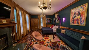 A room with a large TV, a chandelier, a sofa, a patterned rug, and a painting on the wall. - Spacious King Suite! Cher inspired unit. (Sturgeon  Bay)