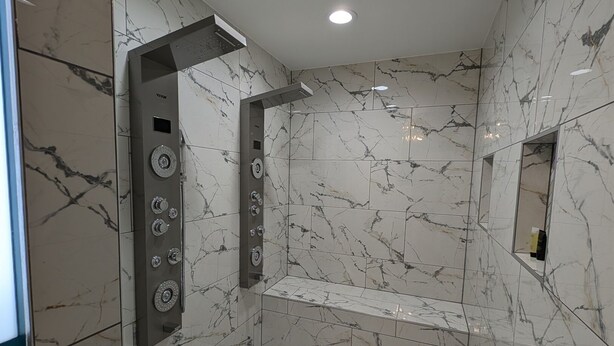 A modern shower with a control panel, marble walls, and a herringbone floor pattern. - Spacious King Suite! Cher inspired unit. (Sturgeon  Bay)