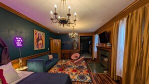 A room with a bed, a sofa, a colorful rug, a chandelier, a fireplace, and a television. - Spacious King Suite! Cher inspired unit. (Sturgeon  Bay)