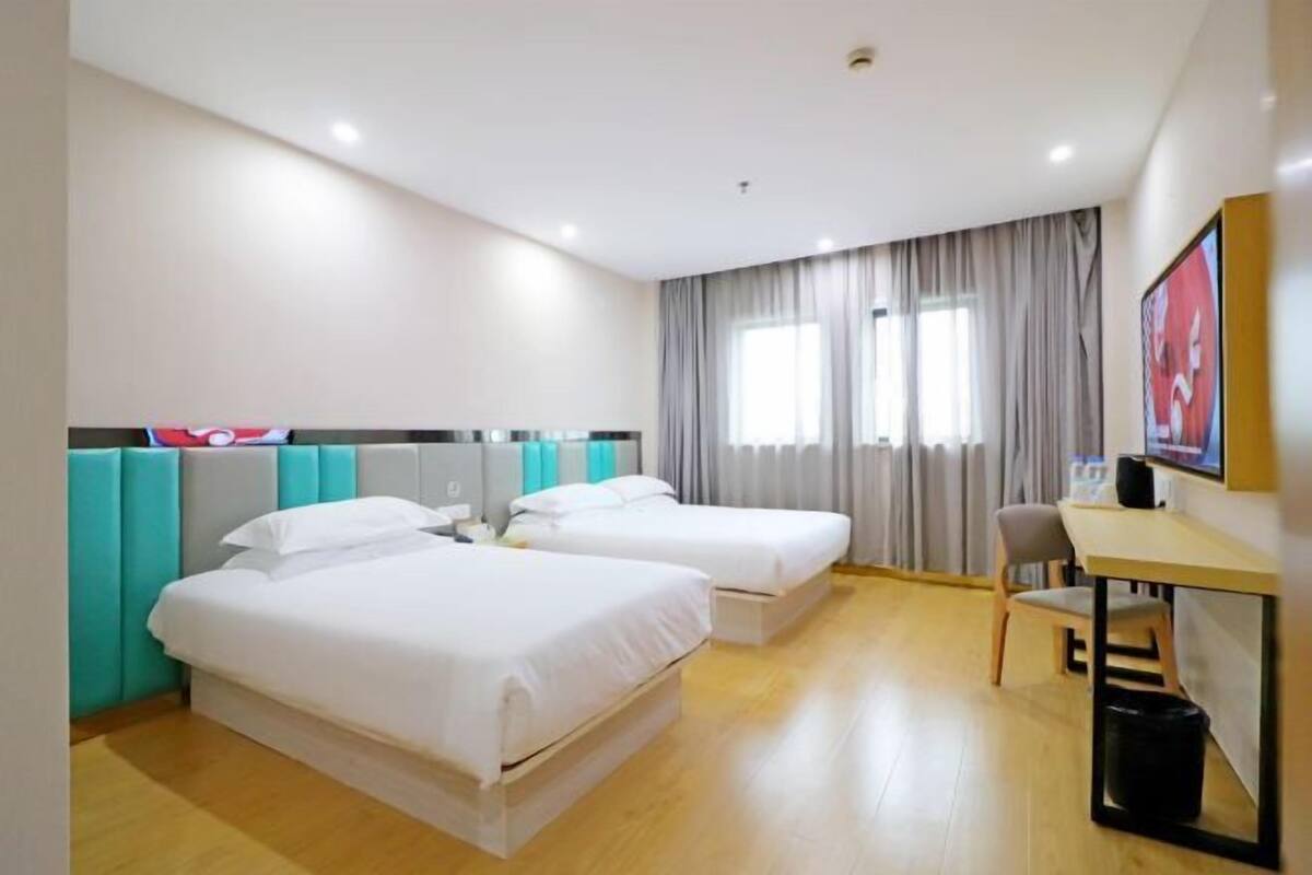 Quarto de hotel com duas camas, uma escrivaninha, uma cadeira e uma janela com cortinas.