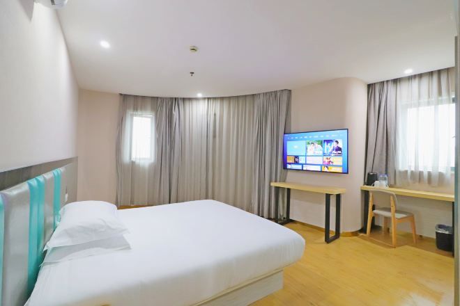 Ett hotellrum med en säng, ett skrivbord, en tv och gardiner.