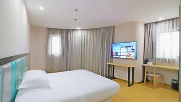Ett hotellrum med en säng, ett skrivbord, en tv och gardiner.